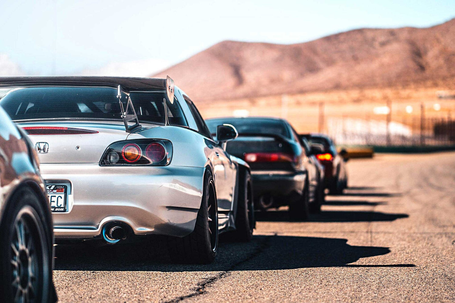 Honda S2000 AP2 with aftermarket rear wing spoiler, titanium exhaust and aftermarket wheels and tires behind an Acura Integra with exhaust